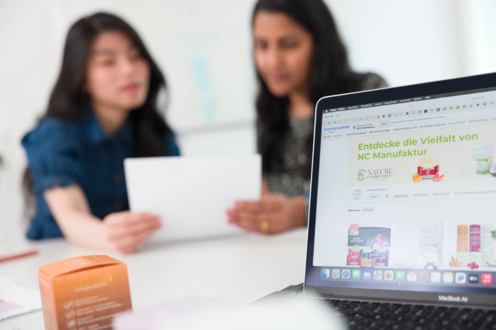 Produktvielfalt auf Laptop im Hintergrund zwei Frauen